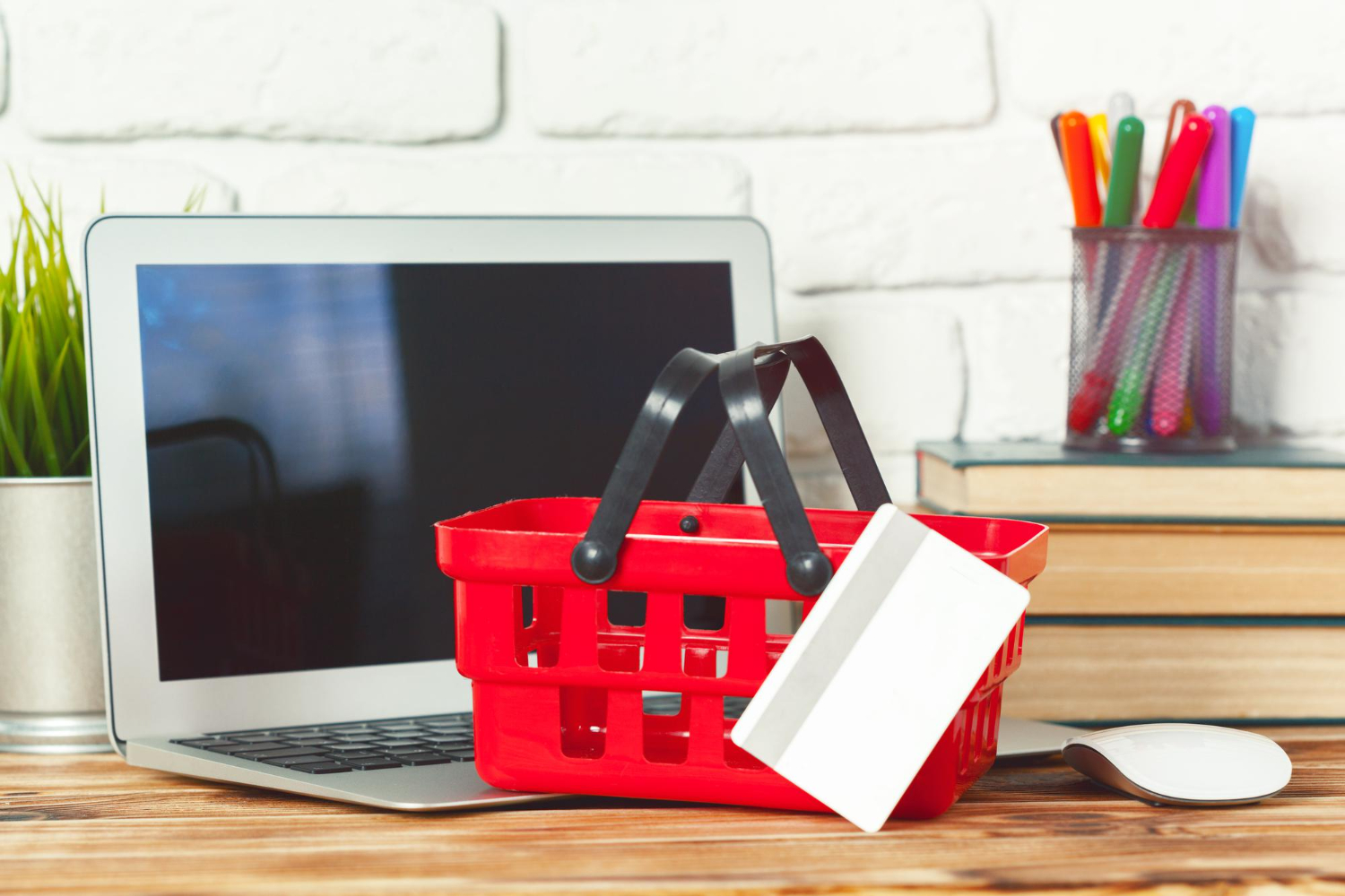 A laptop, shopping basket, and book neatly arranged on a desk.