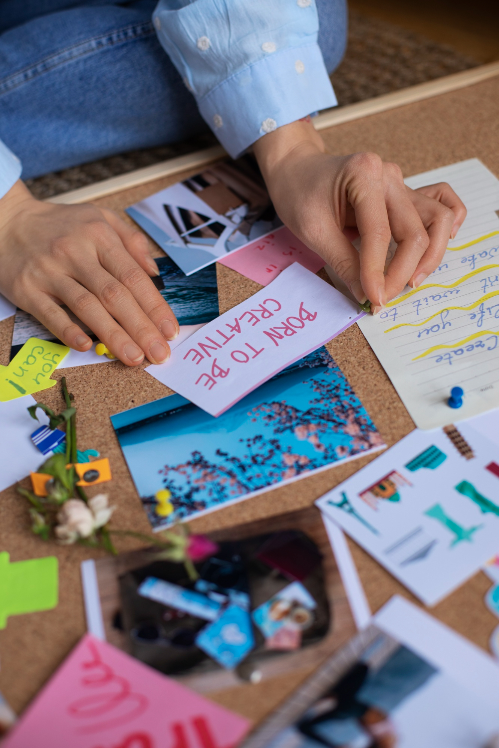 Close-up of a person's hands pinning a note on a cork board covered with photos and assorted notes.